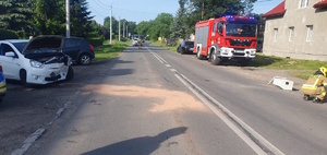 na zdjęciu fragment drogi, na której rozbity biały pojazd, wóz strażacki i strażacy