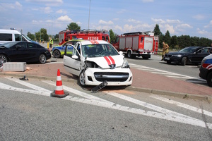 na zdjęciu biało czerwony uszkodzony samochód na drodze, obok inne pojazdy i wozy strażackie