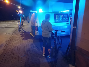 na zdjęciu mężczyzna przy rowerze obok radiowozu, który ma włączone niebieskie światła