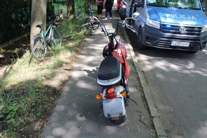 na zdjęciu motorower na chodniku, obok na jezdni radiowóz