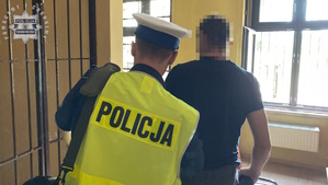 na zdjęciu policjant prowadzi mężczyznę w komendzie