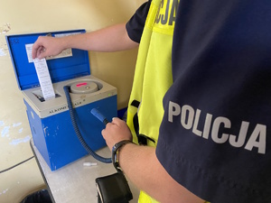 na zdjęciu fragment policyjnego munduru oraz ręka policjanta trzymająca w ręku wydruk a alkomatu