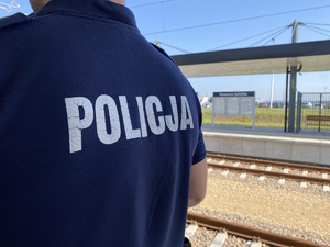 na zdjęciu plecy policjanta z napisem policja, za nim torowisko kolejowe
