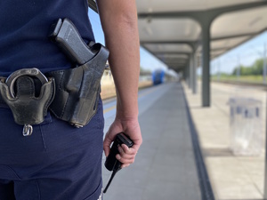 na zdjęciu ręka policjanta, w której trzyma radiotelefon, widoczny także pas główny umundurowania, na którym widoczna broń i kajdanki