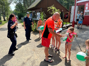 na zdjęciu ratownik wodny rozdaje dzieciom gadżety, obok stoi policjantka i policjant