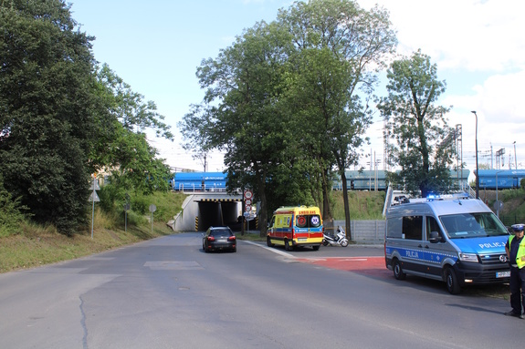 na zdjęciu fragment drogi, na której stoi policyjny radiowóz, karetka pogotowia, motocykl i policjant