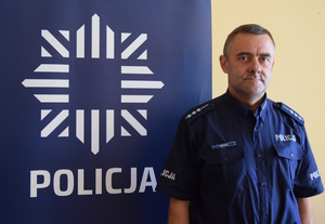 dzielnicowy stoi obok policyjnego baneru, na którym znajduje się gwiazda, a pod nią napis Policja