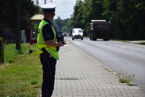 na zdjęciu policjant z miernikiem prędkości przy jezdni, po której jadą samochody