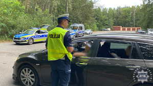 na zdjęciu policjant przy samochodzie, za nim radiowozy i parking