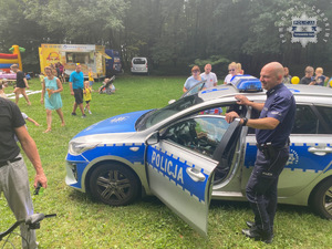 na zdjęciu policjant przy radiowozie, wokół którego stoją dzieci i ich rodzice