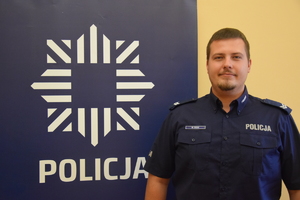 na zdjęciu dzielnicowy Cichy przy banerze z napisem policja