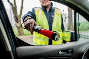 na zdjęciu policjant z alkomatem w ręku skierowanym do wnętrza samochodu od strony kierowcy