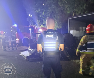 na zdjęciu policjant na miejscu akcji gaśniczej, gdzie obok widoczne budynki i strażacy