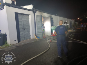 na zdjęciu budynki, a przed nimi policjant i strażacy