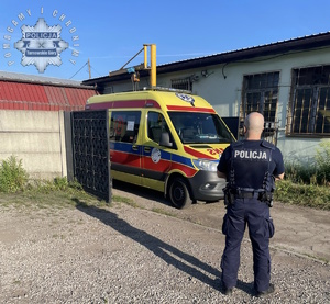 na zdjęciu policjant przed karetką pogotowia, która stoi między ogrodzeniem
