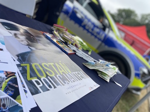 na zdjęciu ulotka z napisem zostań policjantem, w oddali widoczny radiowóz