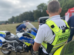 na zdjęciu policjant w odblaskowej kamizelce przy policyjnym motocyklu