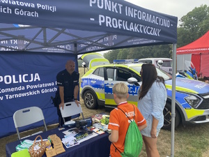 na zdjęciu policjant pod namiotem informacyjnym, a przed nim kobieta z dzieckiem