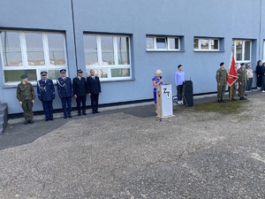 na zdjęciu dyrektor szkoły przy mównicy, obok nie sztandar i przedstawiciele służb