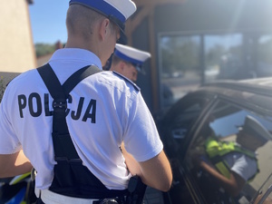 na zdjęciu policjant tyłem do obiektywu przy pojeździe