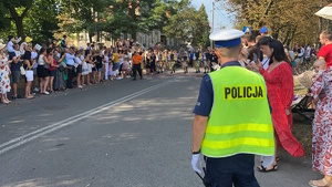 na zdjęciu policjant przy publiczności na pochodzie, gdzie w oddali młodzież idzie z napisem gwarki