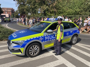 na zdjęciu policjantka przy radiowozie na jezdni, za nim publiczność obserwująca pochód