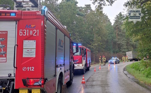 Na zdjęciu wozy strażackie i radiowóz zaparkowane na jezdni przy nich strażacy