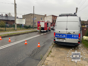 Na zdjęciu Zamknięta droga na chodniku radiowóz na jezdni wóz strażacki i Strażak