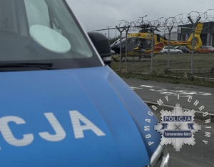 na zdjęciu fragment radiowozu, za którym stoi śmigłowiec lotniczego pogotowia ratunkowego