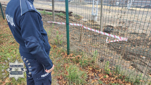 Na zdjęciu policjant przy ogrodzeniu, za którym taśmą wydzielona jest część terenu, na której ujawniono niebezpieczny przedmiot