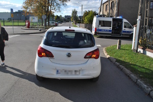 na zdjęciu biały samochód osobowy na drodze, za nim radiowóz na skrzyżowaniu