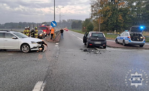 na zdjęciu skrzyżowanie, na którym stoją dwa rozbite pojazdy, za którymi strażacy i inne osoby, obok radiowóz z otwartym bagażnikiem