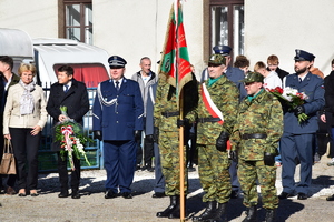 na zdjęciu poczet sztandarowy, za nim komendant policji, przedstawiciele służby więziennej, burmistrz miasta i inne osoby