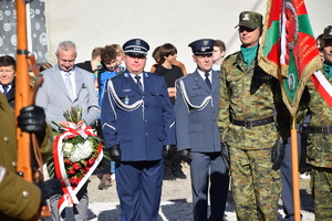 na zdjęciu komendant powiatowy policji w towarzystwie funkcjonariusza służby więziennej, obok inne osoby, a przed nimi poczet sztandarowy