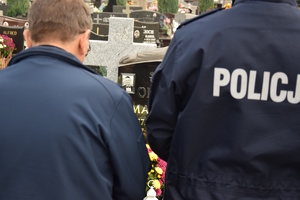 na zdjęciu policjant i kapelan tyłem do obiektywu, spomiędzy nich wyłania się zdjęcie zmarłego umieszczone na nagrobku