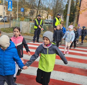na zdjęciu dzieci przechodzące przez jezdnię, na chodniku policjanci