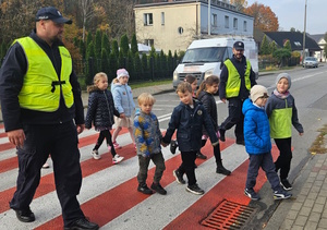 na zdjęciu policjanci przeprowadzający dzieci przez przejście dla pieszych