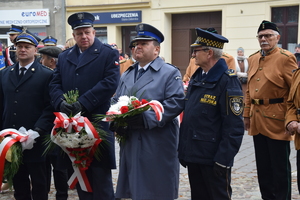 na zdjęciu Komendant Policji z wiązanką kwiatów w rękach, w towarzystwie przedstawicieli innych służb