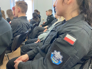 na zdjęciu widoczna siedząca w auli młodzież z ubrana w mundury z naszywkami flagi biało czerwonej i naszywką klasa policyjna szóste liceum ogólnokształcące w Tarnowskich Górach