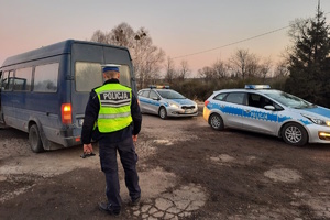 na zdjęciu policjant, przed nim bus i dwa radiowozy