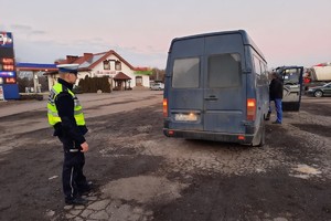 na zdjęciu policjant, przed nim bus, z tyłu budynek stacji benzynowej