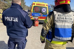 na zdjęciu policjant i strażak, a przed nimi karetka pogotowia ratunkowego