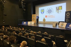na zdjęciu policjant na scenie przed uczniami na widowni