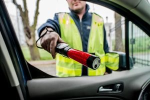 na zdjęciu policjant kierujący do wnętrza samochodu urządzenie do badania trzeźwości