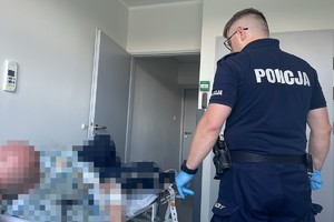 na zdjęciu policjant obok łóżka szpitalnego, na którym leży mężczyzna