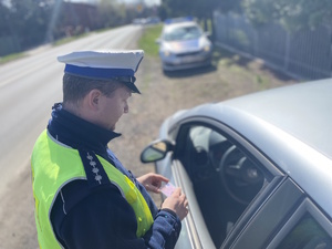 na zdjęciu policjant przy samochodzie, za nim w oddali radiowóz