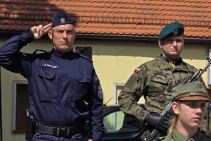na zdjęciu policjant oddający honor w trakcie warty honorowej, stojący obok żołnierza z bronią