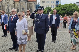 na zdjęciu komendant powiatowy w trakcie oddawania honoru, obok niego inne osoby na płycie rynku