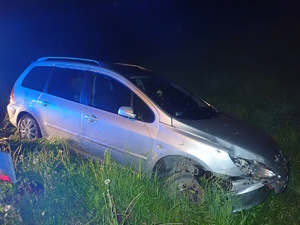 na zdjęciu srebrny samochód na trawniku przy jezdni z widocznymi uszkodzeniami