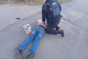na zdjęciu leżący na ziemi zatrzymany, obok niego policjant